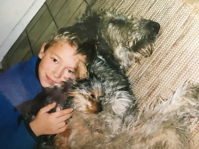 Robin als Junge liegt lächelnd zwischen seinen beiden grauen, zotteligen Hunden.