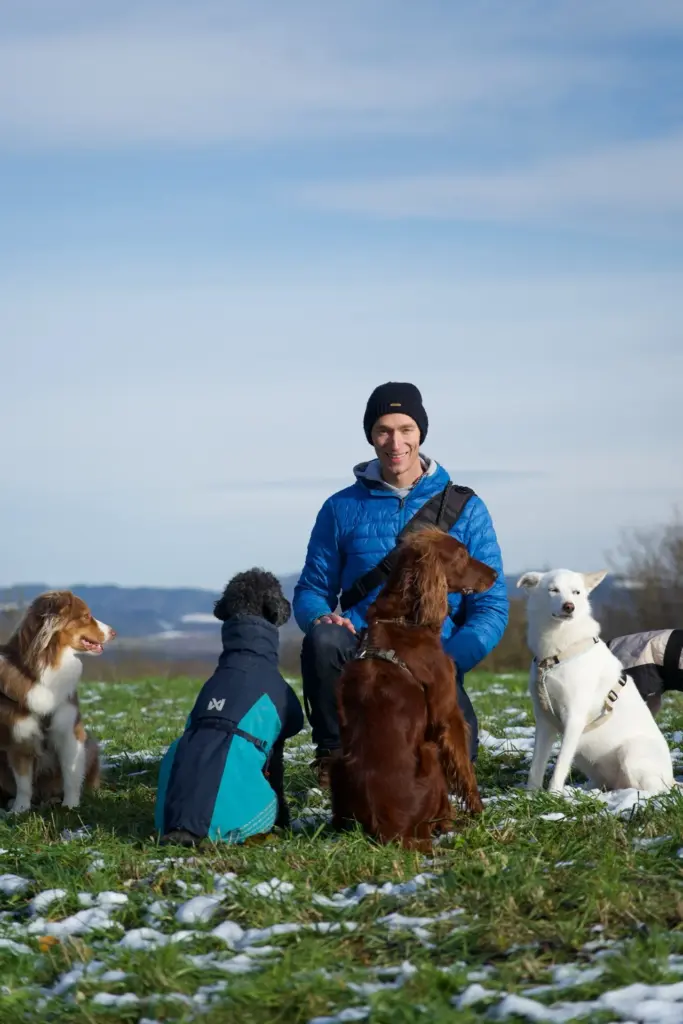 Robin Tast sitzt im Winter auf einer Wiese, umringt von mehreren Hunden beim Sozialspaziergang.